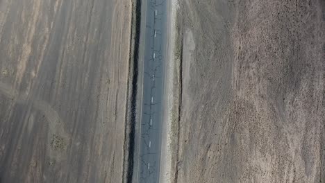 Aerial-drone-shot-of-car-driving-on-a-desertic-road-from-top